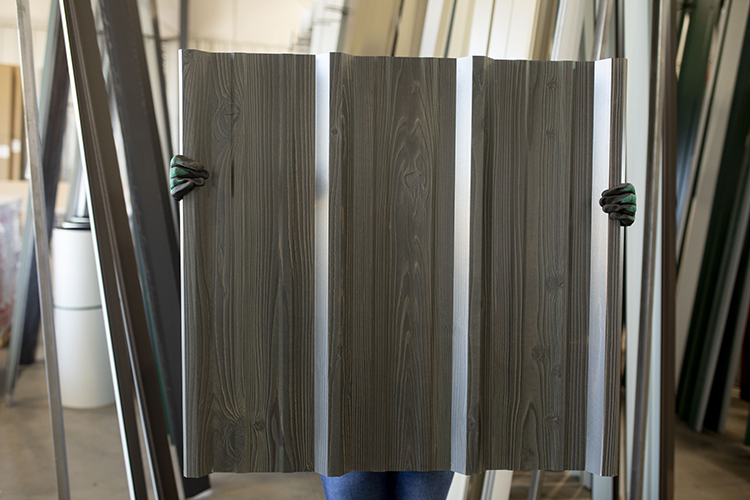 A Metal America worker hold up a 26 gauge steel panel with a wood look finish