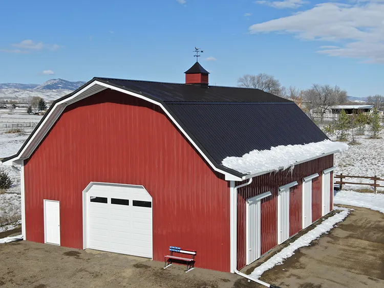 An agricultural building with red metal siding and black metal roofing panels